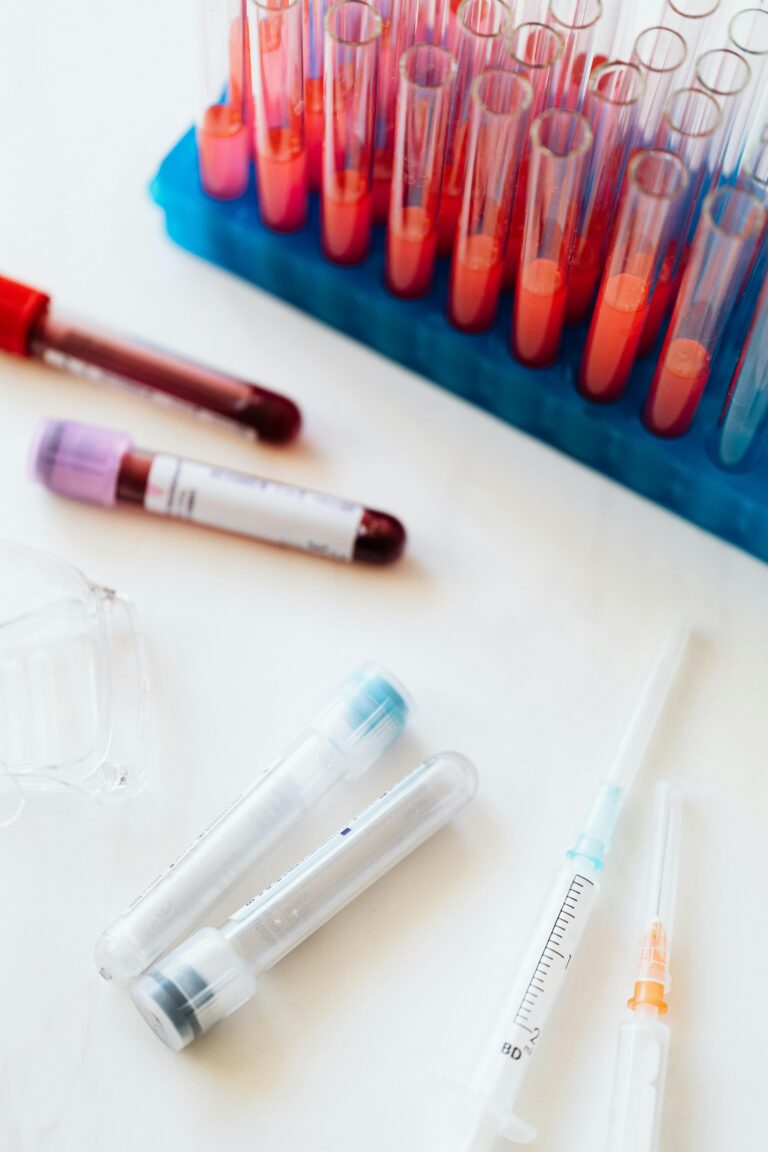 From above of full glass test tubes on plastic container and empty and full of blood plastic vials and syringe placed on white surface
