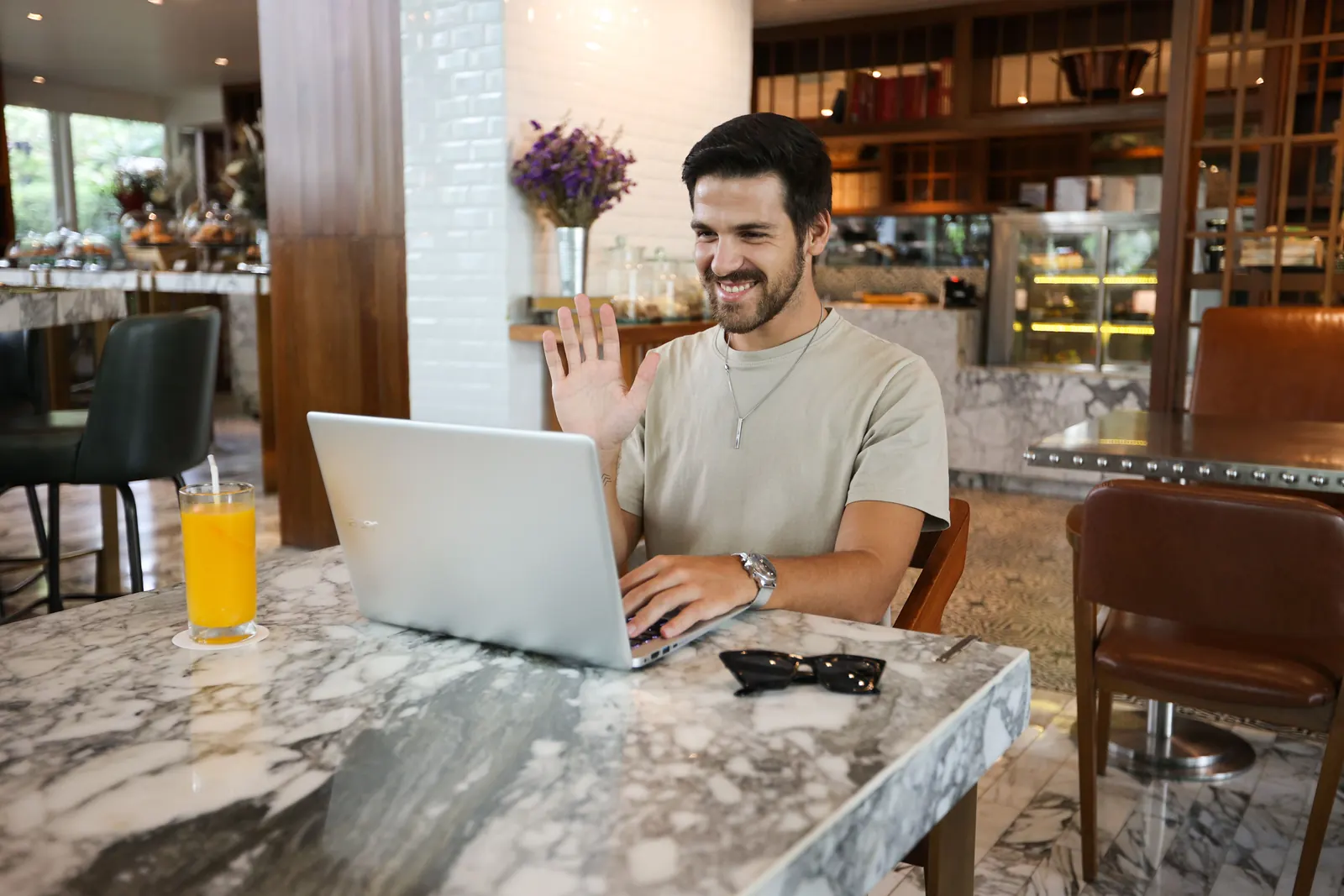 Man waving during a video call on his laptop at a cafe table