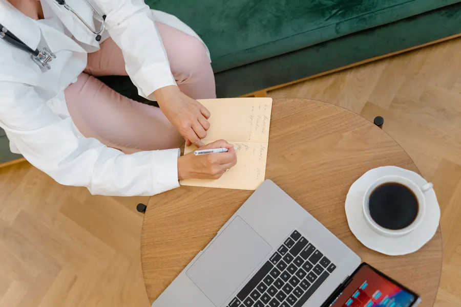 Overhead view of a clinician writing notes beside a laptop and coffee