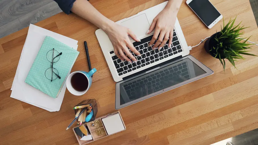 Overhead view of hands typing on a laptop at a wooden desk