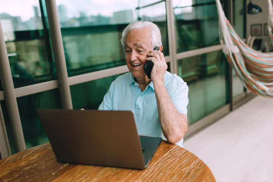 Older man on a phone call while using a laptop at home