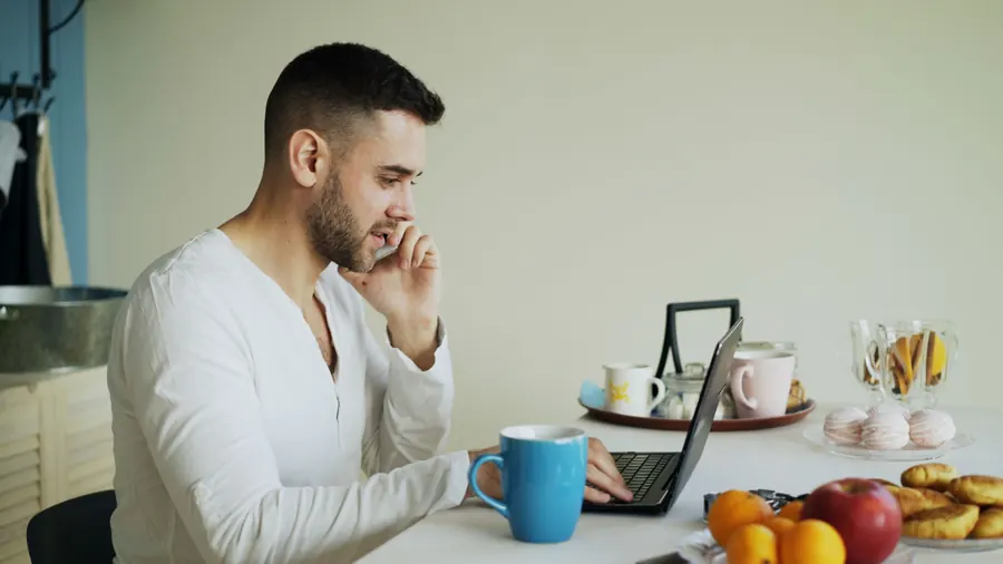 Man on a phone call while working on a laptop at home