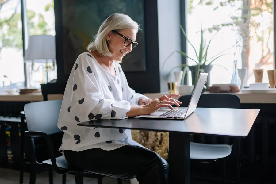 Woman in a polka dot blouse working on a laptop by a window